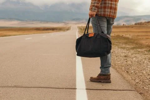 Man with bag in hand walking down a mountain road Stock Photos