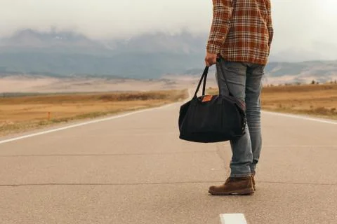 Man with bag in hand walking down a mountain road Stock Photos
