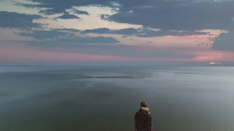 The man with bag standing on the mountain cliff on the seascape background Video stock 143033335
