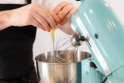 Man baker cooking a cake by adding egg in the navy blue food processor machine, Stock Photos