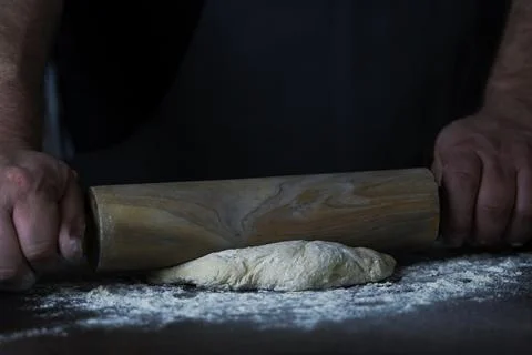 Man Baker or chef is rolling fresh dough with a dough roller on a wooden surf Stock Photos