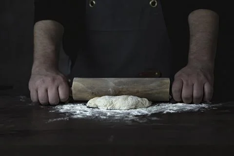 Man Baker or chef is rolling fresh dough with a dough roller on a wooden surf Stock Photos