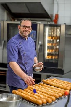 Man baker in uniform baking baguettes with bread shelves on background 스톡 사진