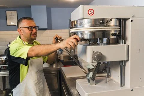 Man baker using a press machine to make pizza, modern bakery machine, bakery Stock Photos