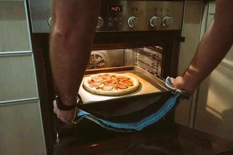 A man bakes pizza at home using an oven. Men's hands pull a pizza baking sheet Stock Photos
