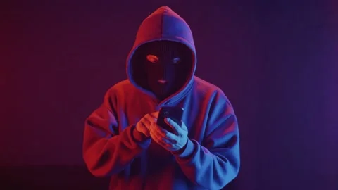 Man in a balaclava in a dark room talking on a smartphone Stock Footage 201603652