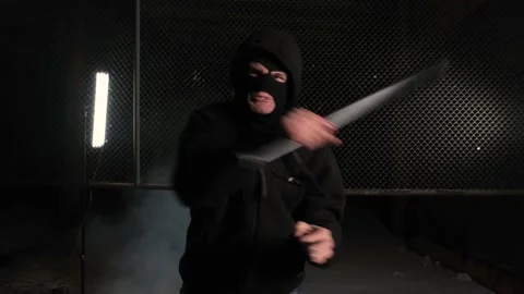 A man in a balaclava strikes with a baseball bat in front of the camera at night Stock Footage 169154477