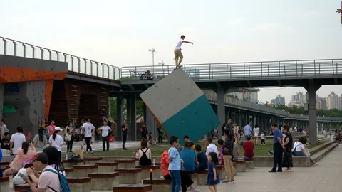 Man Balances on Top of Big Cube Structure in Shanghai with People Around, Day Stock Footage 123049124