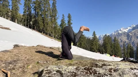 Man balancing in sirsasana on grassy patch with snow covered landscape and .. Vídeos de archivo 333701085