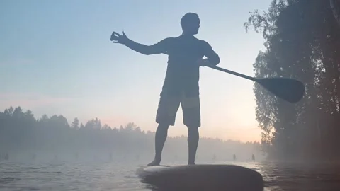 Man balancing on surf board with paddle Stock Footage 164891231