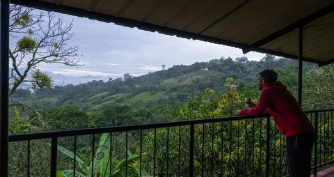 Man on Balcony Drinking Coffee While Looking Over Lush Mountain Landscape Foto stock