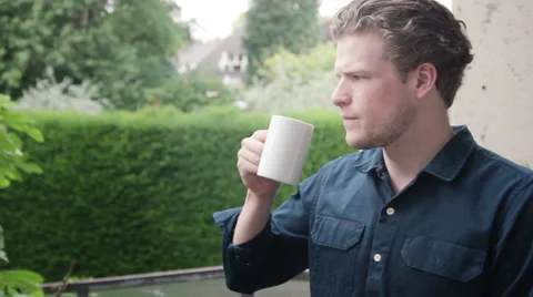 Man on balcony, drinking from cup, looking into his garden Stock Footage 40662353