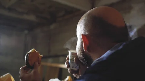 Man with a bald head drinks tea from a disposable cup and eats a bun Stock Footage 102942152