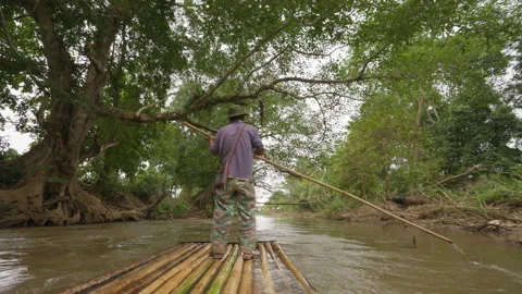 Man on bamboo raft using a long bamboo pole to push his raft Stock Footage 232471445