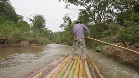 Man on bamboo raft using a long bamboo pole to push his raft Stock Footage 232471884