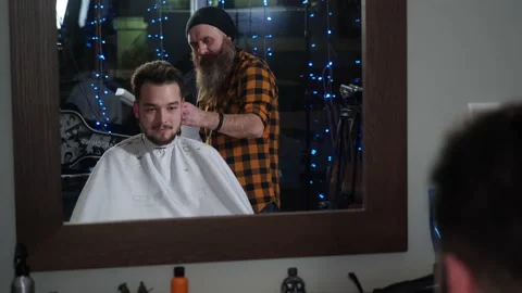 A man barber with a long beard makes a haircut typewriter to a young man client Stock Footage 147704900