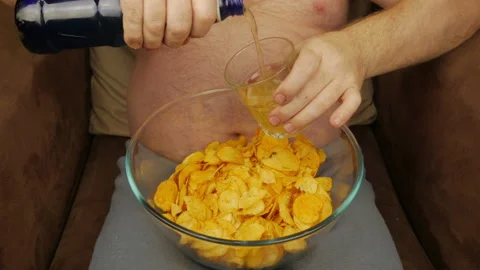 A Man With A Bare Belly Drinks Beer And Eats Chips Stock Footage 147549936