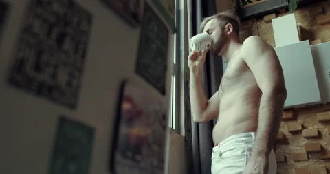 A man with a bare torso serves coffee at the apartment window. Slow motion. Stock Footage 144815605