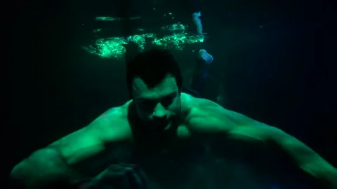A man with a bare torso swims up to the camera and swims away in the dark water Stock-Footage 206637090
