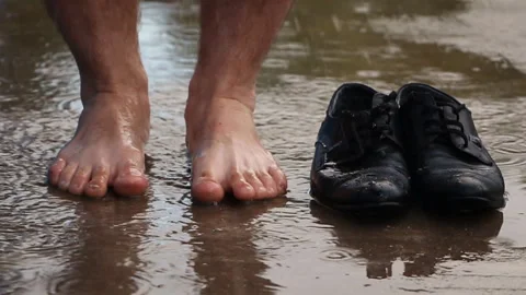 A man barefoot jumps in a puddle on the pavement near his shoes Stock Footage 108438285