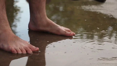 Man barefoot in a puddle on the pavement stands near his shoes Stock Footage 108435984
