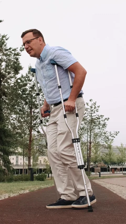 A man barely hobbles on one leg with crutches. Adult male walking slowly down Stock Footage 301015481