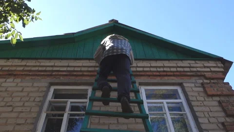 A man in a baseball cap and a plaid shirt carefully descends the wooden Stock Footage 210359523
