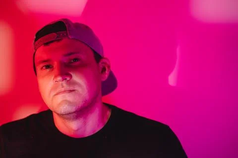 Man in baseball cap looking at camera under neon pink light. Serious young ma Stock Photos