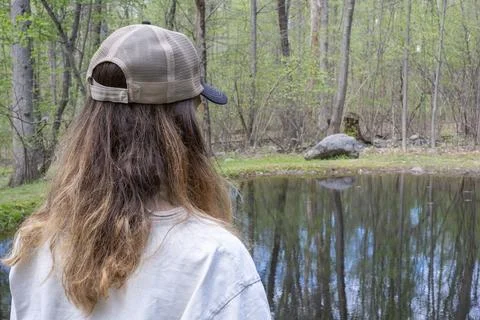 Man in Baseball Cap Looking at Reflective Forest Pond Stock Photos