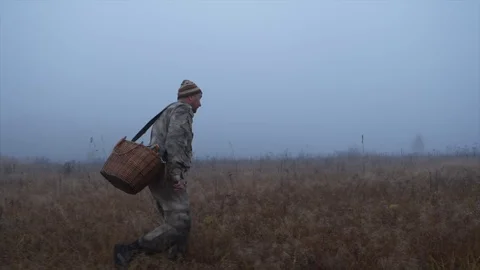 A man with a basket is walking across the field among the fog Stock Footage 124209406