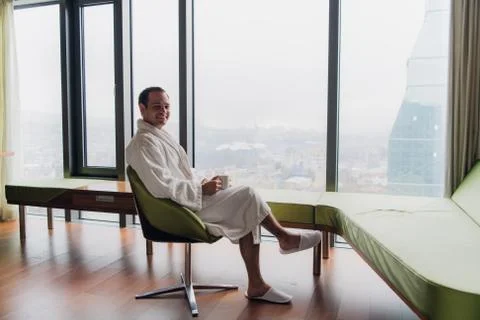 Man in bathrobe drinking coffee, looking at cityscape Stock Photos
