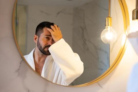 Man in bathrobe looking at himself in the mirror. Stock Photos