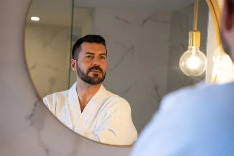 Man in bathrobe looking at himself in the mirror. Stock Photos