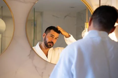 Man in bathrobe looking at himself in the mirror. Stock Photos