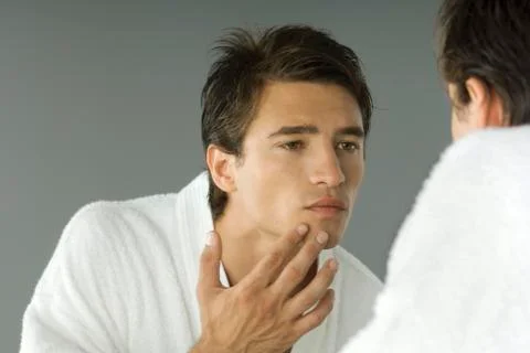 Man in bathrobe looking in mirror, inspecting skin Stock Photos