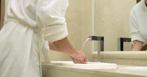 Man in bathrobe presses button to run water and washes face Video stock 141050957
