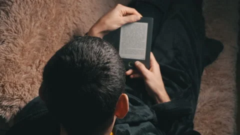Man in a Bathrobe Reads an E-book While Sitting on the Couch Stock Footage 171375794