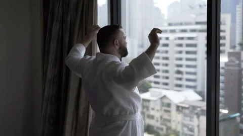 Man in bathrobe walking to the window and stretching his muscles  Stock Footage 88437448