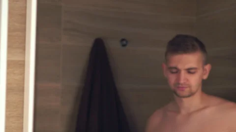 Man in the bathroom brushing his teeth morning and looks in a mirror Vídeos de archivo 85636499