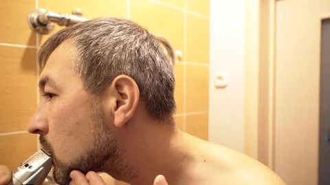 The man in the bathroom in front of the mirror cuts his beard with a trimmer. Stock Footage 82236808