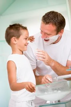 Man in bathroom putting shaving cream on young boy's nose Stock Photos
