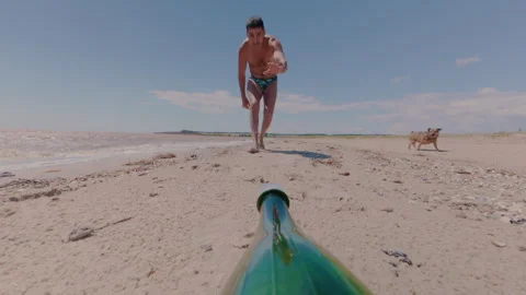 A man on the beach approaches a lying bottle and greedily drinks water from it. Vidéo 339930632
