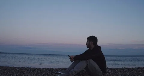 Man on the beach chatting with his smart phone during a sunset Stock Footage 125945786