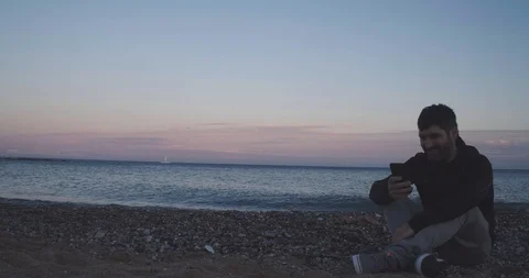 Man on the beach chatting with his smart phone during a sunset Stock Footage 125946590
