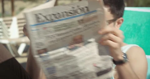 Man on the beach stops reading newspaper and takes sunglasses off Video stock 205026649