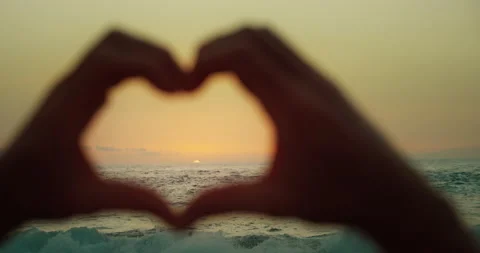 Man on beach at sunset making figure of heart with fingers. Hands in shape of Stock Footage 239590411