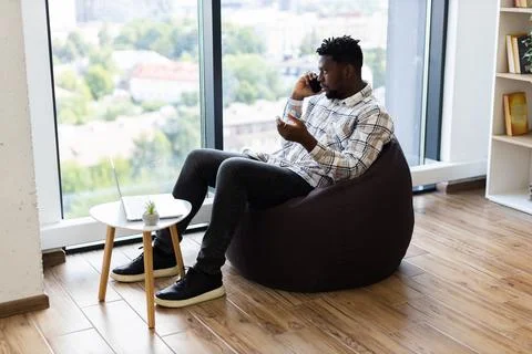 Man in bean bag using smartphone during work session by large window Stock Photos