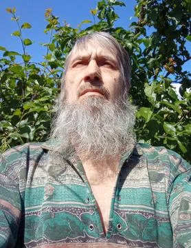 A man with a beard against a background of a green tree and blue sky. Kind face. Stock Photos
