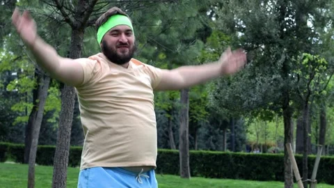 Man with beard and beige t-shirt jumping and clapping in city park Stock Footage 307997568