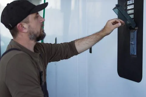 Man with beard and cap inserts a coin into a self-service car wash payment .. Stock Photos